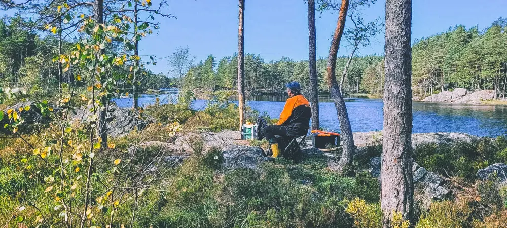 En mann sitter på en stolsekk i skogen og speider utover vannet.