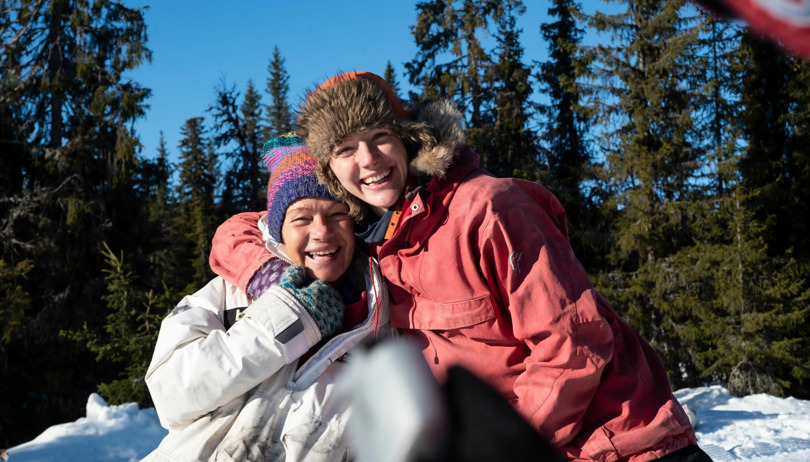 To smilende damer ute i snøen gir hverandre en klem