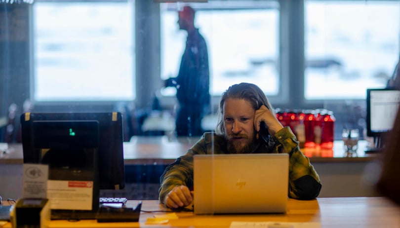 Mann sitter bak en bærbar PC og ser på skjermen mens han holder en mobiltelefon mot øret.