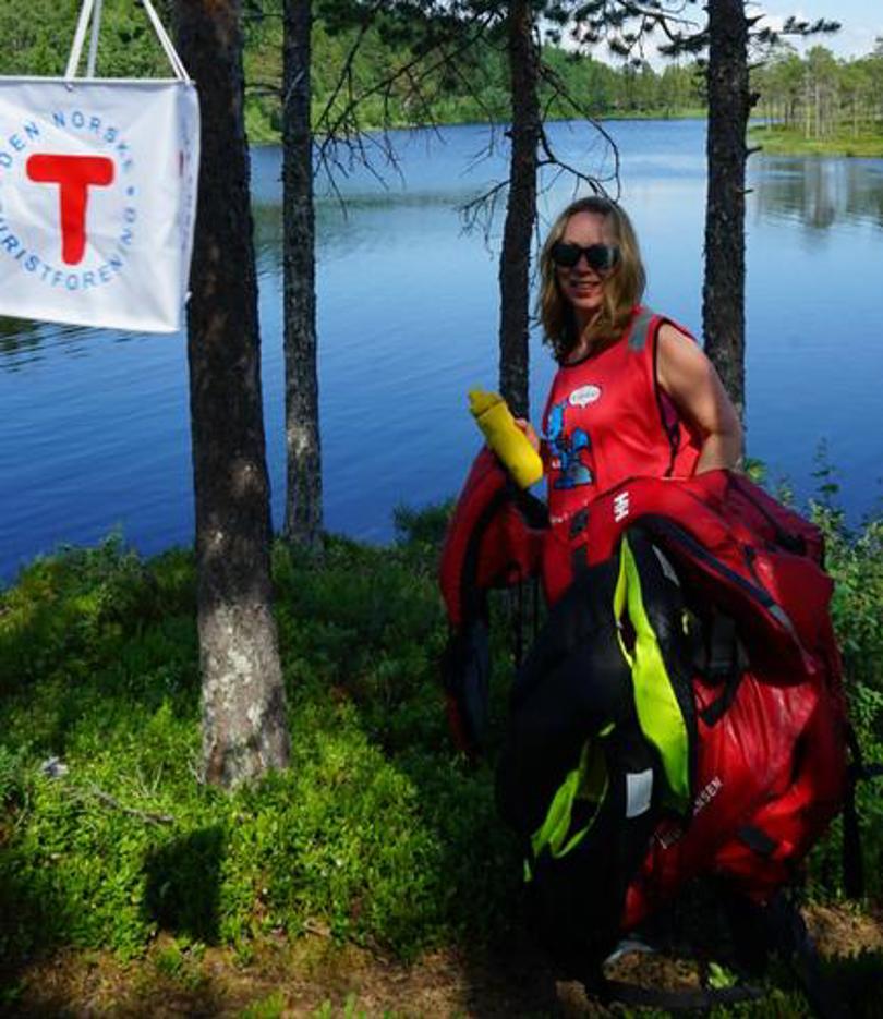 Kvinne med rød T-vest, ved skogsvann.