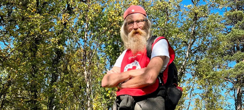 Mann med rød DNT-vest på tur i skogen. Foto.