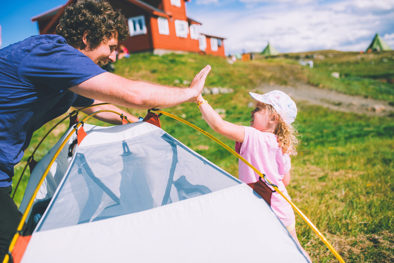 En kvinne og en liten jente gjør en high-five over noe som ligner på et telt, med en rød hytte i bakgrunnen