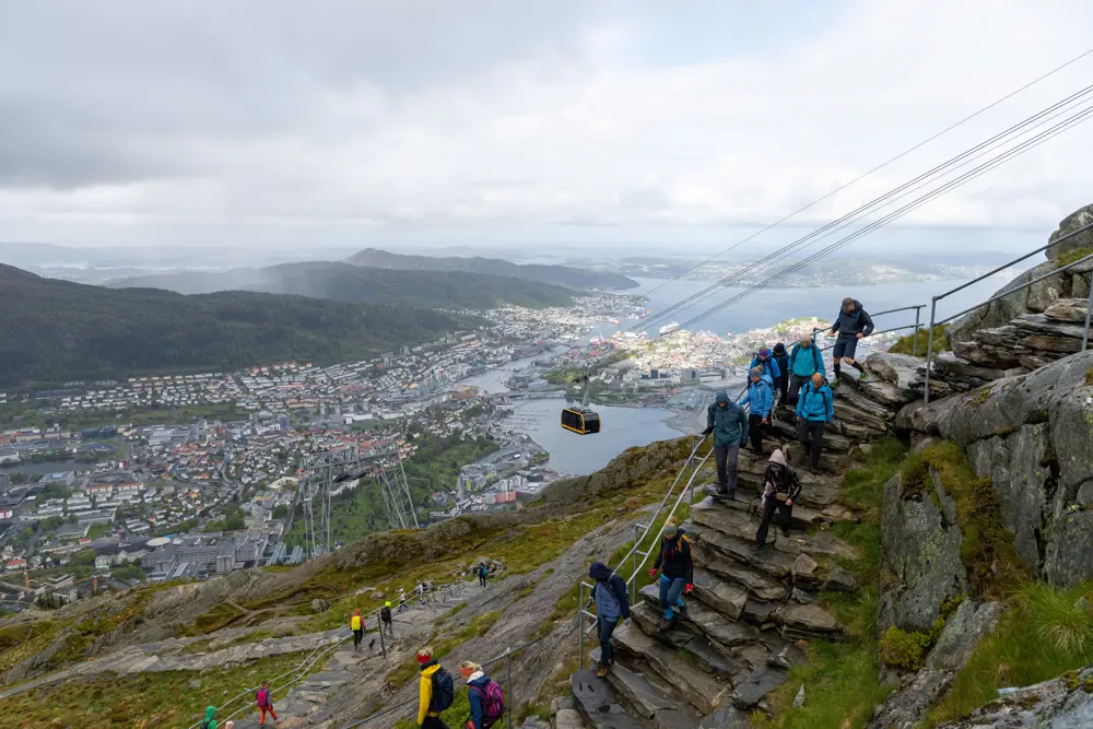 Mange turgåere går ned en steintrapp med utsikt over Bergen i bakgrunnen.