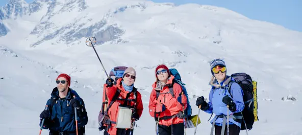 Gruppe på ski blant snøkledde fjell.