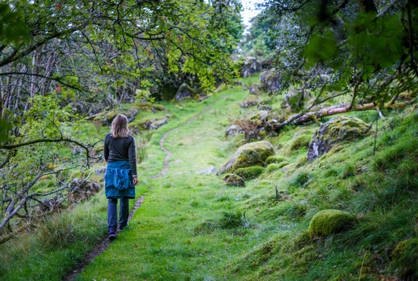 En kvinne går med ryggen til nedover en gress-sti i en skog.