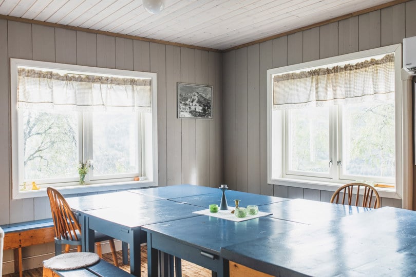 Stort og blått kjøkkenbord i et grått rom med to vinduer.