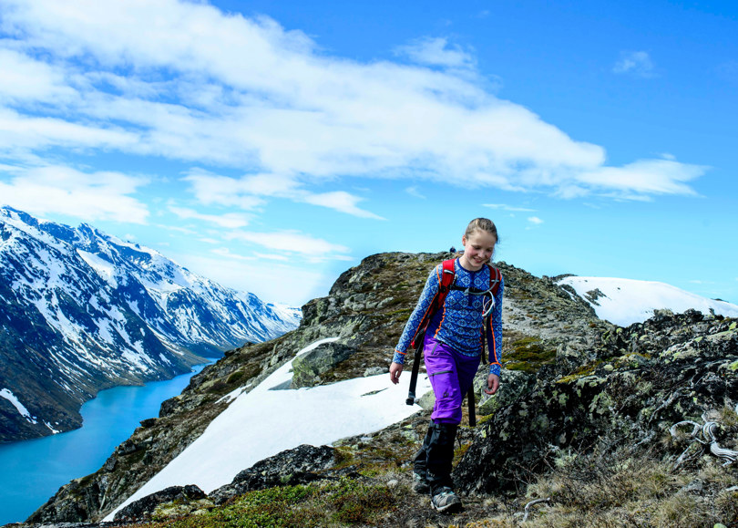 Jente i blå genser og lilla bukse går på fjell med snøflekker.