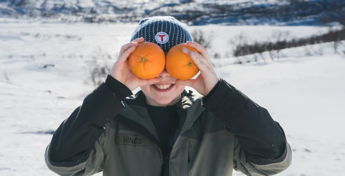 Gutt som holder to appelsiner foran ansiktet