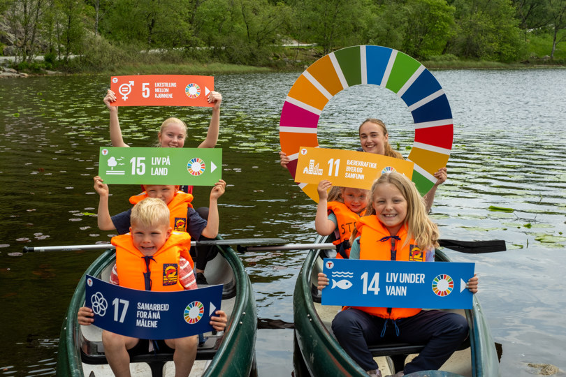 Fem barn som sitter i to kanoer og holder oppe plakater med FNs bærekraftsmål på.