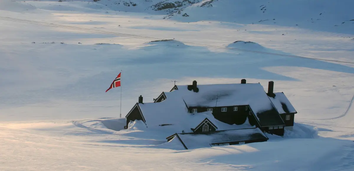 En hytte dekket i snø og med en flagg som svanger i flaggstangen