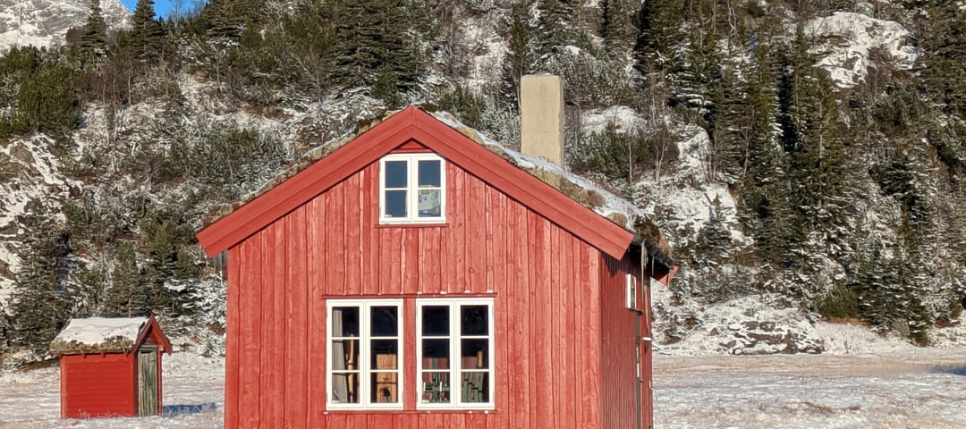 Kvanndalen. Rød hytte bader i sol. Det er litt snø på bakken. 