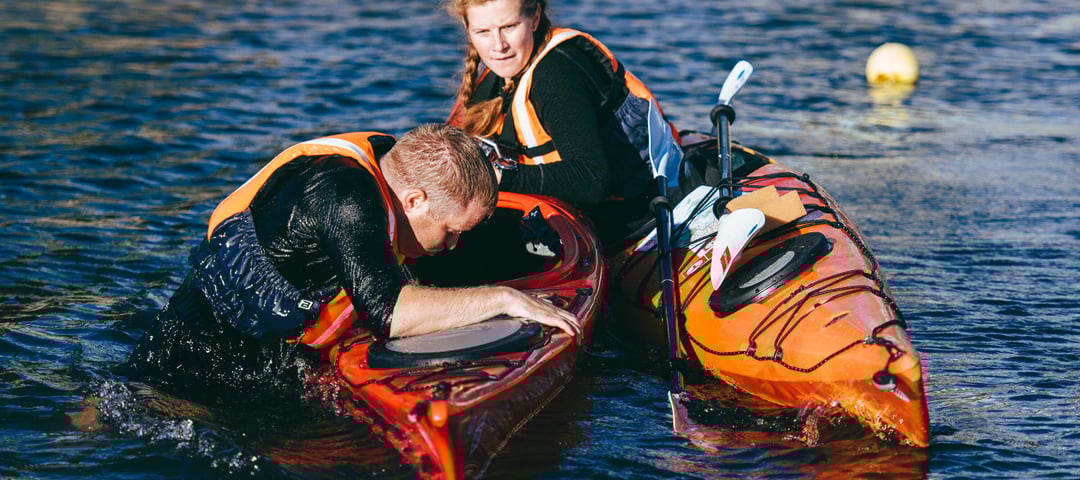 To kajakkpadlere på sjøen, en ruller rundt