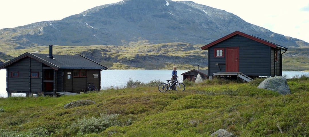 To hytter ved vann med fjell i bakgrunnen