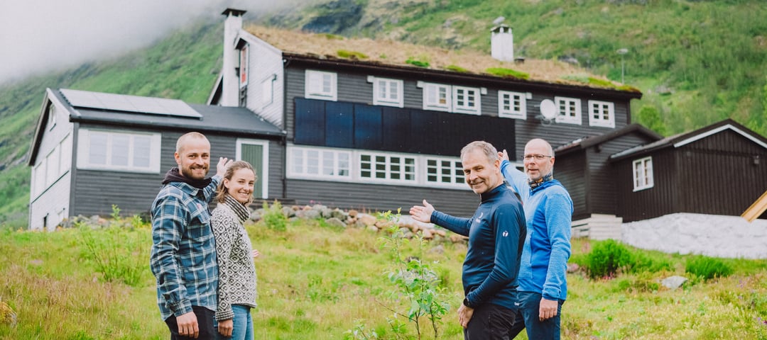 Fire personer foran DNT hytta Skogadalsbøen. Peker stolt på nye solceller på tak og vegger.