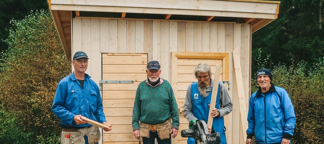 Fire menn i arbeidstøy utenfor en nybygd utedo. Foto.