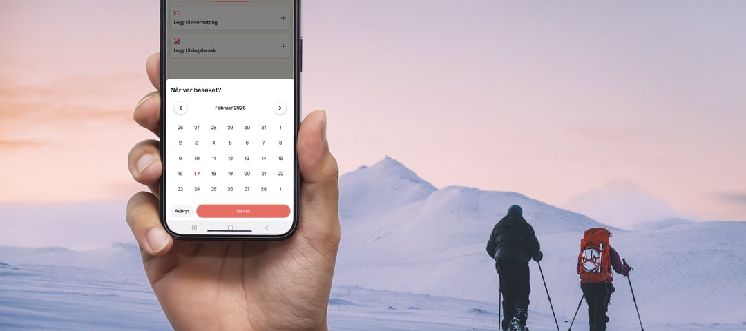 Hånd med mobil foran folk som går på ski i vinterlandskap