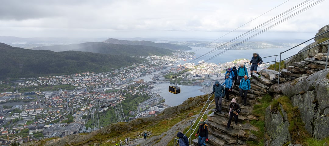 Mange turgåere går ned en steintrapp med utsikt over Bergen i bakgrunnen.