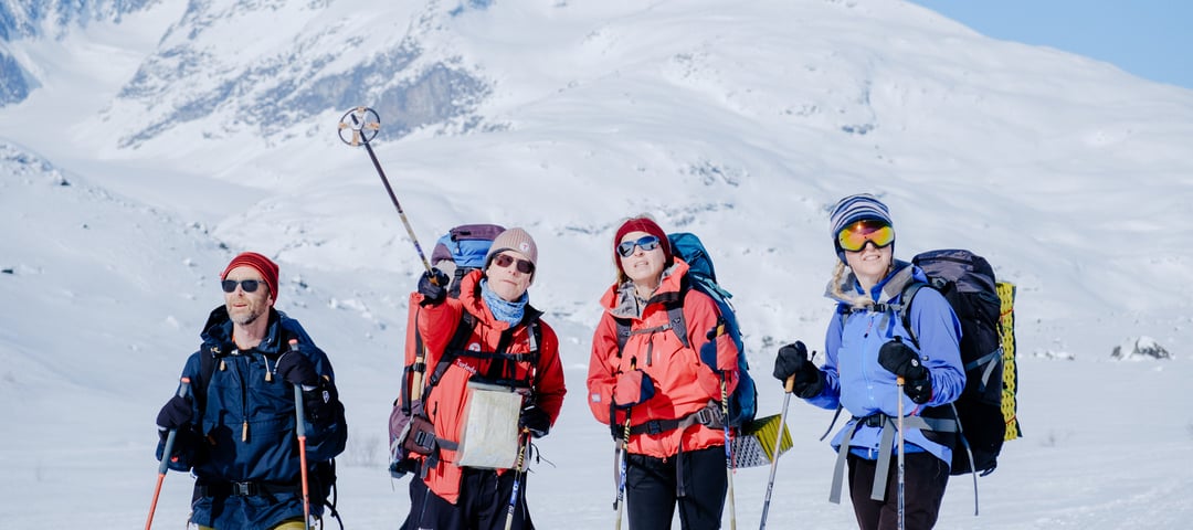 Gruppe på ski blant snøkledde fjell.