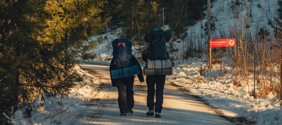 To personer med sekk som går tur på en grusvei dekket av snø