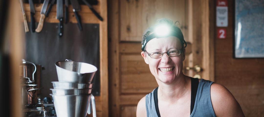 En kvinne med hodelykt dukker opp fra en kjøkkenbenk på en hytte og smiler.