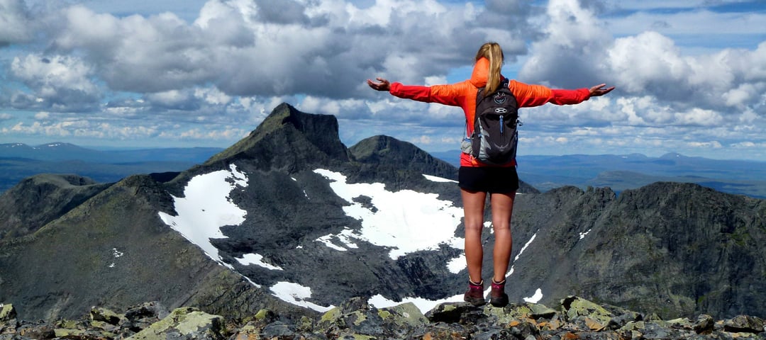 Person står med armene utstrakt og ser vekk fra oss, ut over steinete fjell-landskapet foran oss.