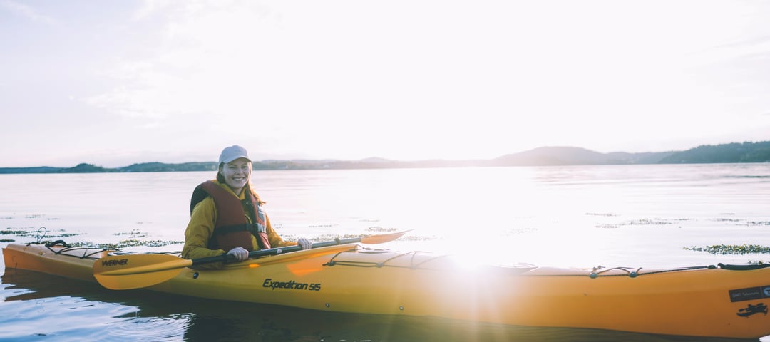 Kvinne som padler kajakk i solnedgang. Foto.