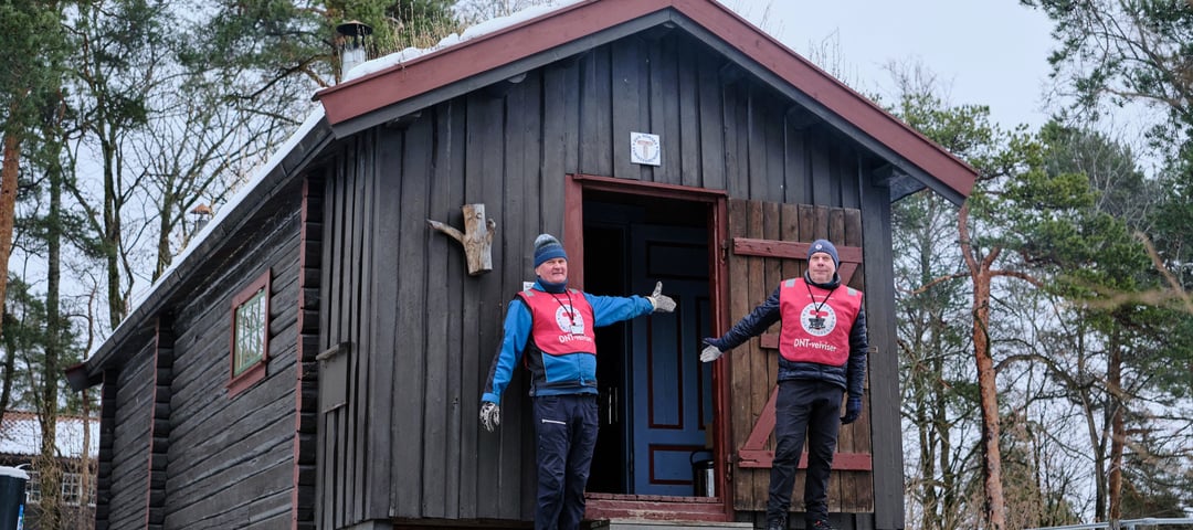 To frivillige fra DNT ønsker velkommen inn i DNT-hytta på Norsk Folkemuseum
