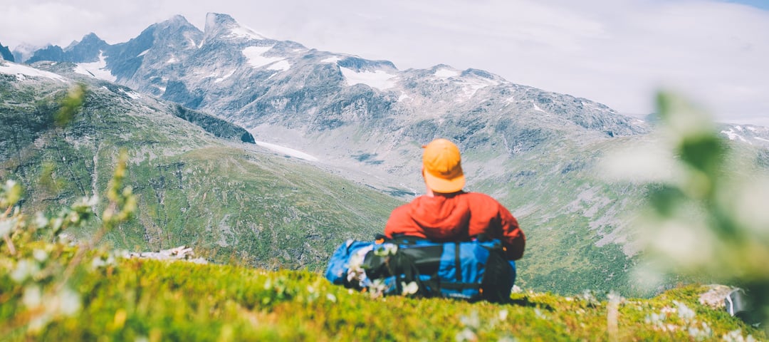 Mann med caps og rød jakke som ser utover fjellet. 