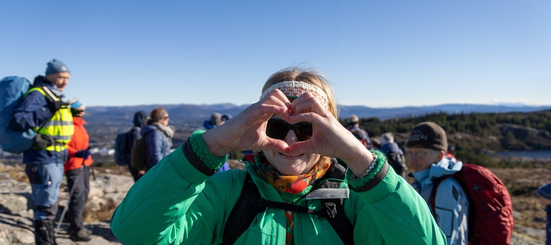 Voksen dame i grønn jakke lager hjerte med fingrene.