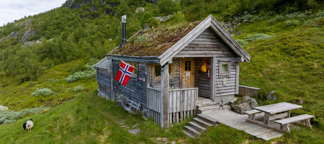 Koselig klassisk hytte med torvtak og norsk flagg utenfor.
