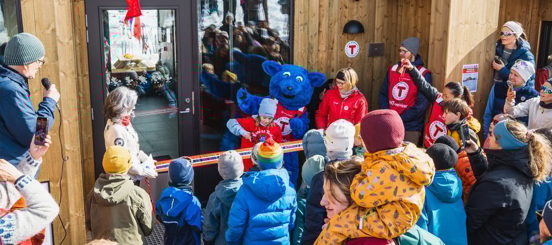 Ei jente klipper snoren foran døren på en ny og moderne hytte. Rundt henne står mange barn og voksne, og Barnas turlag sin maskot, den blå fjellreven Turbo.
