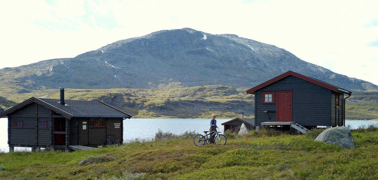To hytter ved vann med fjell i bakgrunnen