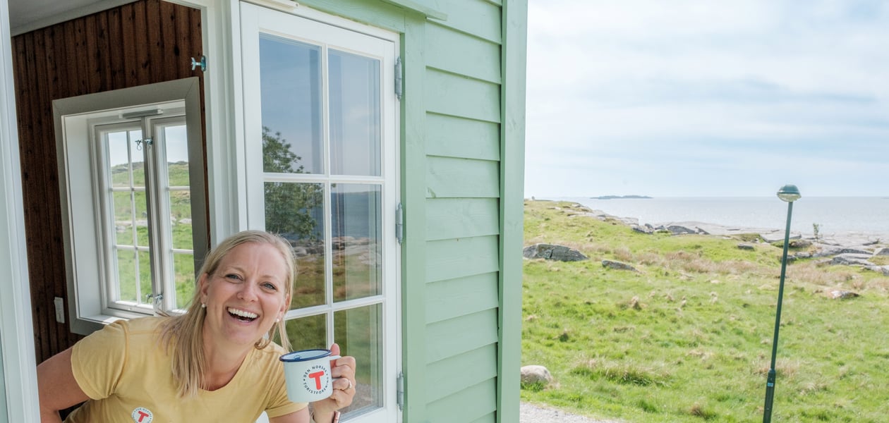 Kvinne smiler i et vindu og holder en kaffekopp