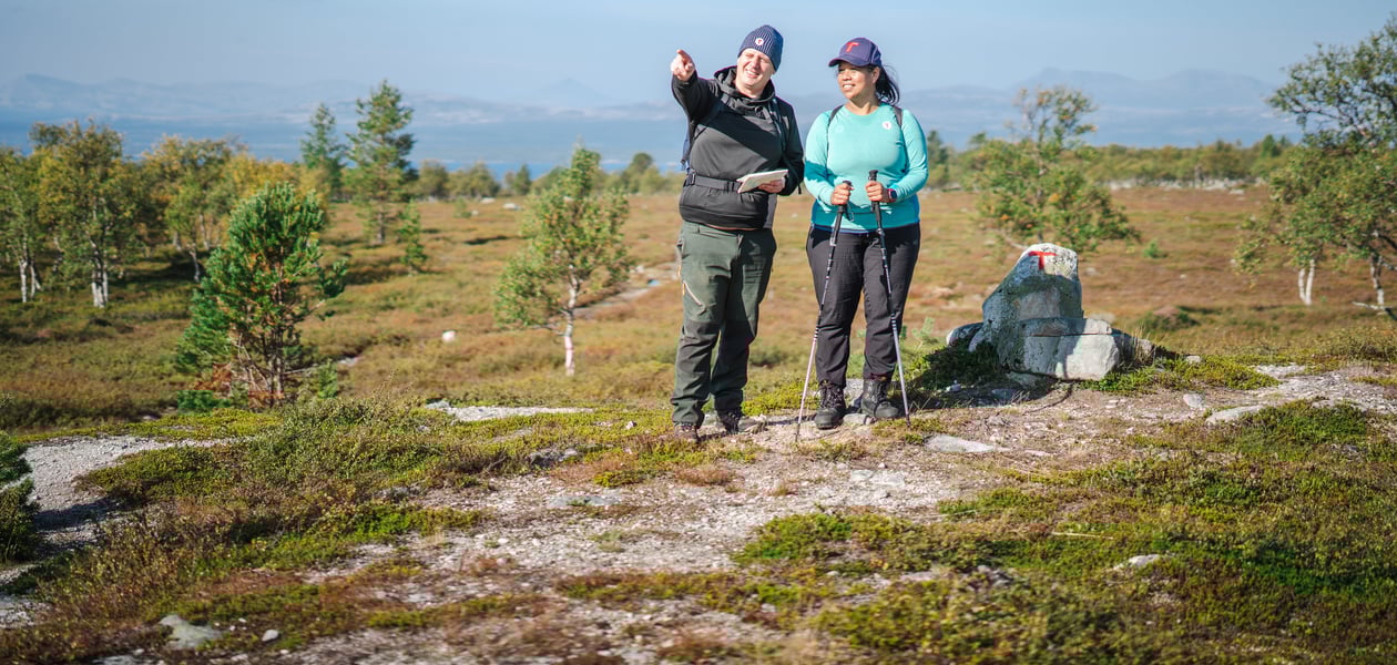 To personer som ser dit mannen peker. De står i et fjellområde, det er blå himmel