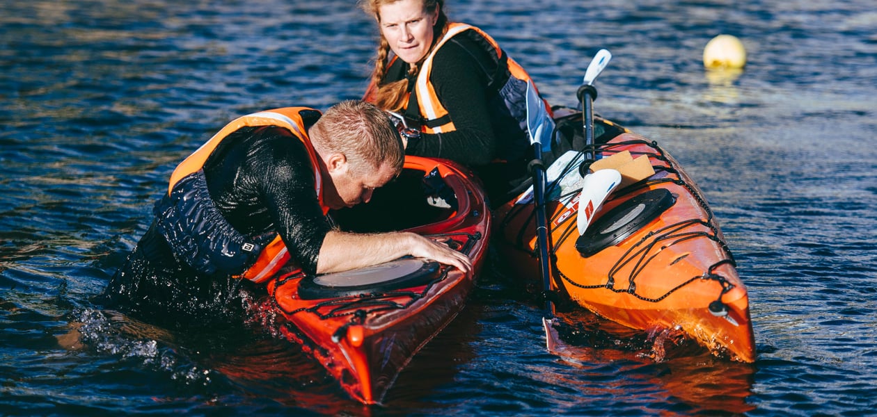 To kajakkpadlere på sjøen, en ruller rundt