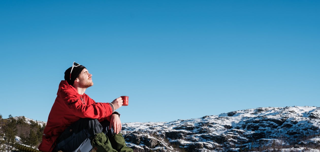 En mann sitter på toppen av et fjell og nyter en kopp kaffe i solen