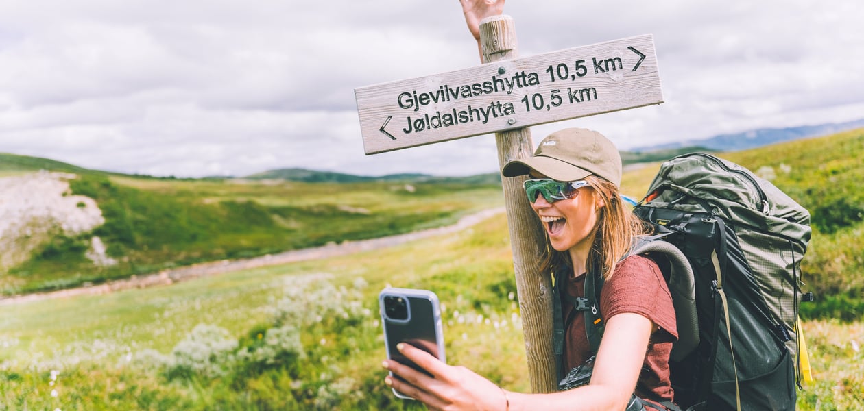 Jente som står og tar en selfie foran en skiltstolpe som viser vei og avstand til Jøldalshytta og Gjevilvasshytta