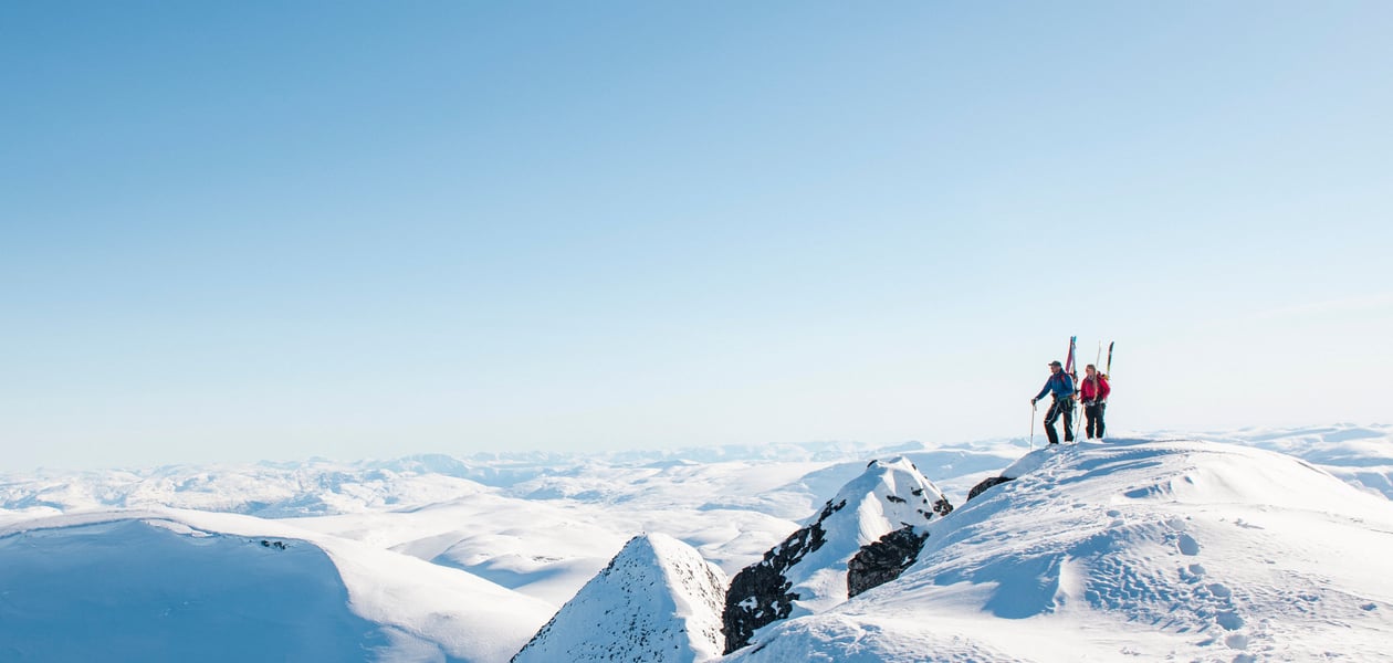 To personer med ski på sekken på en snødekket fjelltopp
