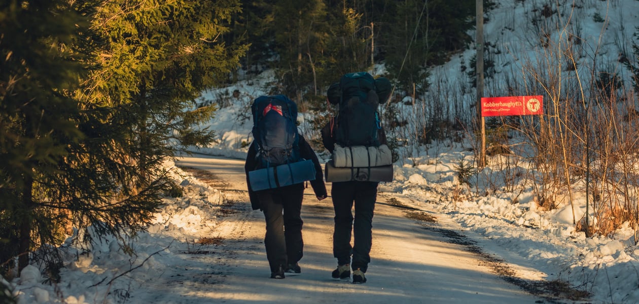 To personer med sekk som går tur på en grusvei dekket av snø