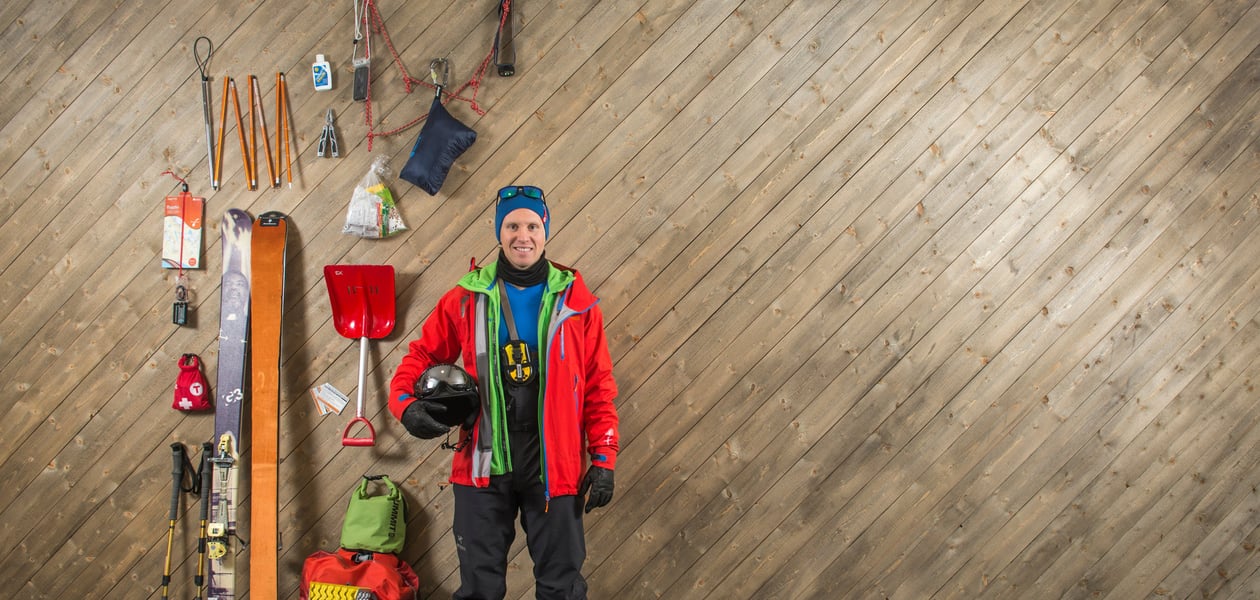 Mann står ved vegg, med utstyr for topptur rundt seg.