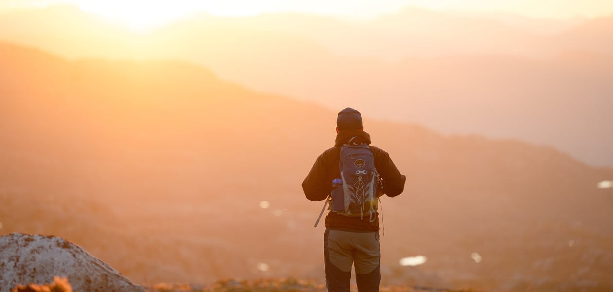 Person som står med ryggen til å speider utover landskapet. Kveldslys.