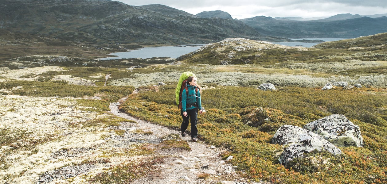Dame med sekk på ryggen som går i fjellet