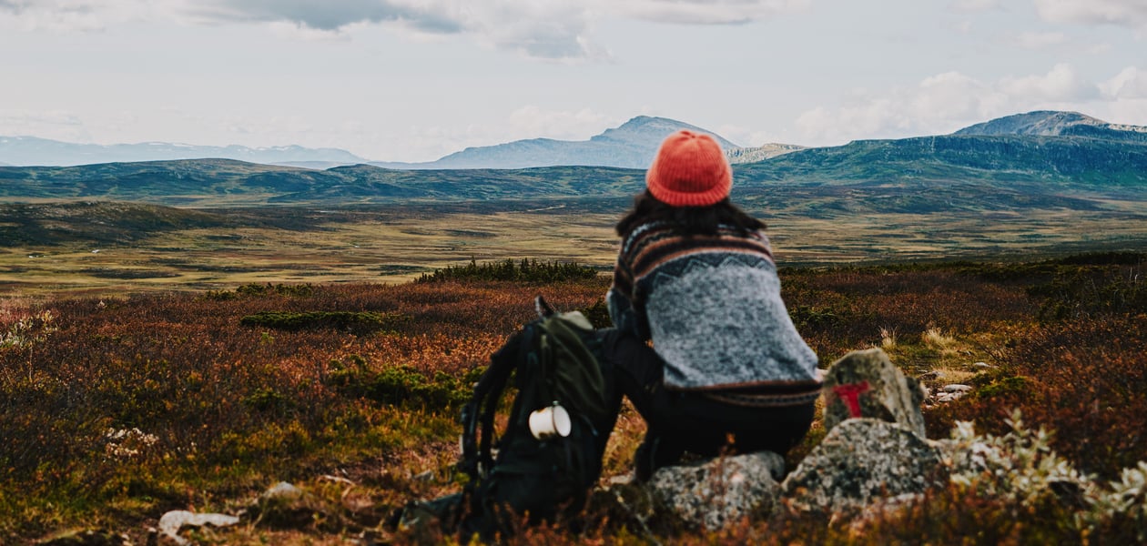 Dame med oransje lue som ser utover et fjellandskap