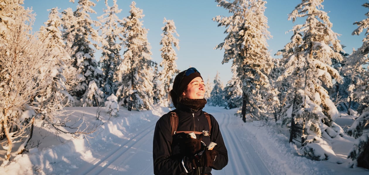 Smilende kvinne på ski i snødekt skog. 