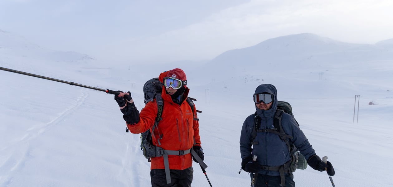 To vinterkledde menn med fullt vintertøy står ute på ski i fjellet.