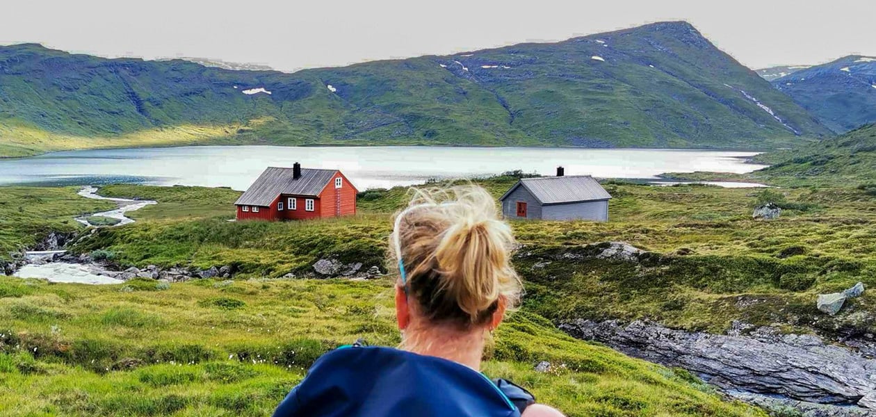 Kvinne med ryggen til kamera ser mot en hytte i det fjerne.