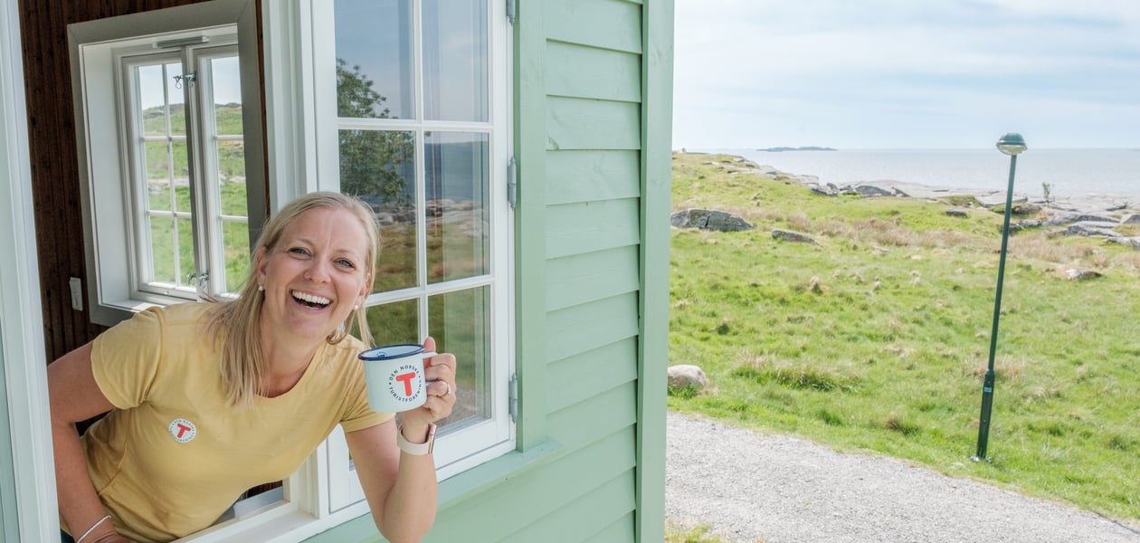 Kvinne smiler i et vindu og holder en kaffekopp