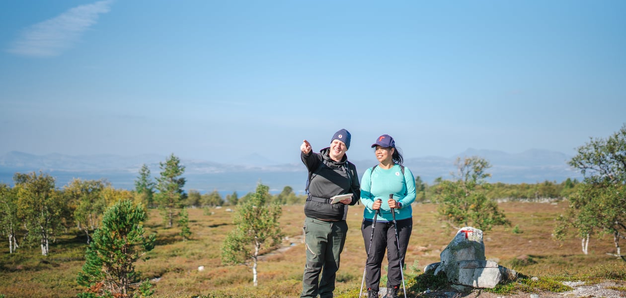 To personer som ser dit mannen peker. De står i et fjellområde, det er blå himmel