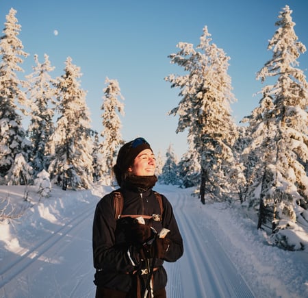 Smilende kvinne på ski i snødekt skog. 