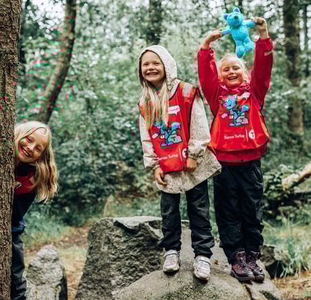 Tre jenter leker i skogen med blå Turbo-bamse